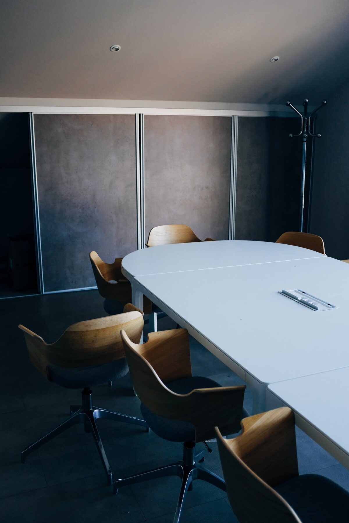 Sala de conferencias con mesa blanca rectangular y sillas ergonómicas de madera en espacio con paredes oscuras